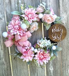 a baby girl wreath with pink flowers and greenery hanging on a wooden fence next to a sign that says baby girl