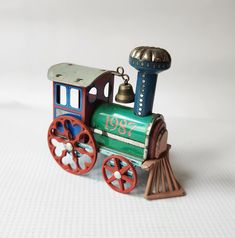 a small toy train sitting on top of a white table next to a metal bell