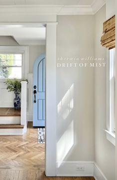 an open door leading into a white room with wood floors and windows in the background