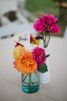 two vases filled with flowers sitting on top of a white tablecloth covered table