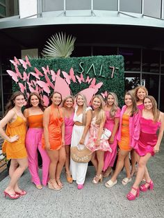 a group of women standing next to each other in front of a pink and orange sign