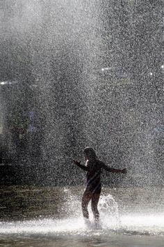 a person standing in the water with their arms spread out and one arm outstretched, as it is raining