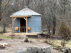 a small blue building sitting in the middle of a forest next to rocks and trees