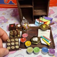 a hand is holding a small wooden box with various items in it on a table