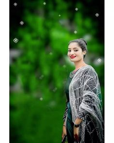 a woman wearing a black and white sari standing in front of green trees with her hand on her hip