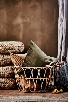 a basket filled with lots of pillows on top of a floor next to a pile of blankets