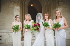 a group of women standing next to each other in front of a building holding bouquets