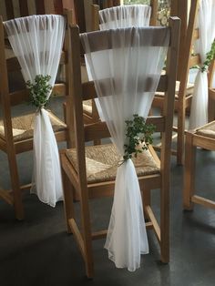 the chairs are covered with white chiffon drapes and tied with greenery