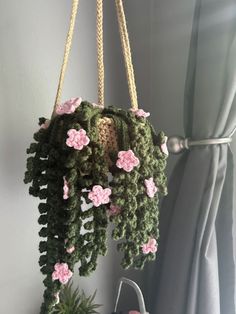 a crocheted hanging planter with pink flowers