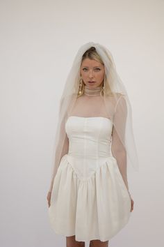 a woman in a white dress and veil posing for the camera with her hands on her hips