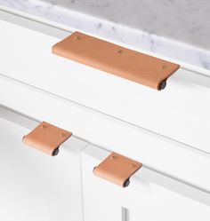 a pair of leather drawer pulls on the side of a white cabinet with marble counter top