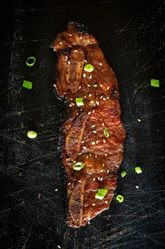 a piece of meat with sesame seeds and green onions on a black surface next to some chopsticks