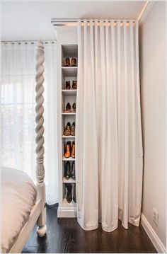 a bedroom with white curtains and shoes on the shelves in front of the bed, next to a window