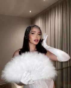 a woman in a white dress and feathered gloves is posing for the camera with her hand on her head