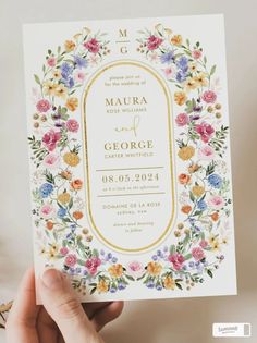 a hand holding up a wedding card with flowers on the front and bottom, in gold foil