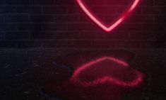 a red heart shaped neon sign sitting on top of a black floor next to a brick wall