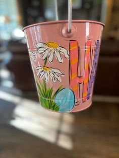 a pink bucket with flowers painted on it hanging from a metal hook in a living room