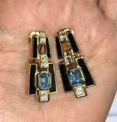 This pair of signed Christian Dior earrings is comprised of gold tone metal and stunning black enameled hinged jeweled door knocker styled dangles. Dating to the 1980s-90s, the earrings are clip ons and are signed on the back of each clip. The earrings have clear rectangular or square shaped rhinestones set into it to accent a beautiful aquamarine colored emerald cut rhinestone. They really are lovely and they appear all original and free of any damage or repair. In very good vintage condition, Christian Dior Earrings, Door Knocker Earrings, Art Deco Revival, Dior Earrings, Aquamarine Colour, Vintage Christian Dior, Christian Dior Couture, Dior Couture, Silver Lights