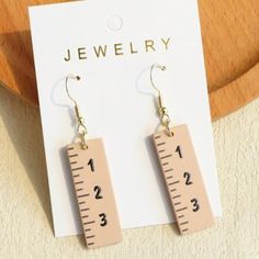 pair of earrings with measuring tape on them sitting next to a piece of paper that says jewelry