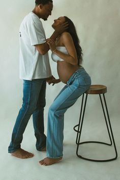 a man standing next to a pregnant woman on top of a stool in front of a white background