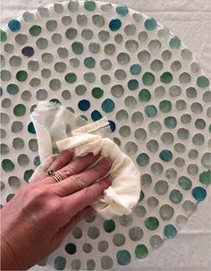 a hand holding a cloth on top of a white plate covered in green and blue circles