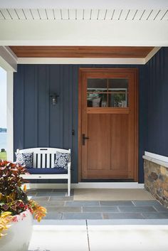 a wooden door sitting next to a white bench on top of a stone floored porch