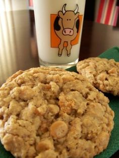 two cookies sitting on top of a green napkin next to a glass of milk and a cow sticker