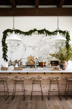 a kitchen with marble counter tops and hanging lights over the island, surrounded by wooden stools