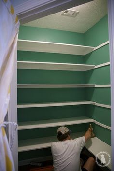 a man is sitting in the corner of a closet with shelves painted green and white