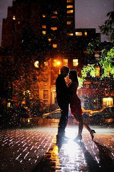 a man and woman dancing in the rain at night with their arms around each other