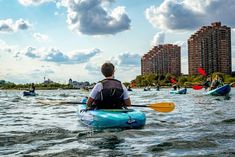 several people in kayaks paddling on the water with buildings in the back ground