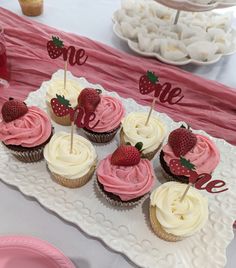 cupcakes with strawberries on top are arranged on a white platter at a party