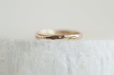 a gold wedding band sitting on top of a white marble slab in front of a white wall