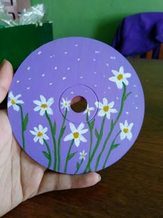 a hand holding a purple painted disc with white daisies on the outside and yellow centers