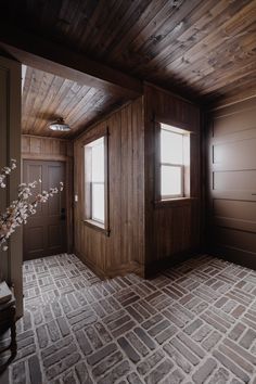 an empty room with wood paneling and brick tiles on the floor, along with two windows