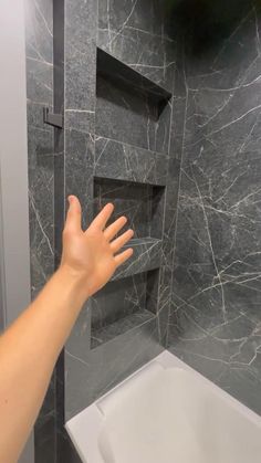 a person's hand reaching for something in a bathroom with marble walls and floor