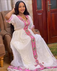 a woman sitting in a chair wearing a white dress with pink trims and beads