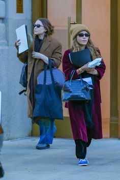 two women are walking down the street carrying bags and folders in their hands,