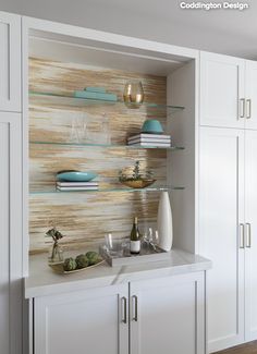 a kitchen with white cupboards and shelves filled with plates, glasses and wine bottles