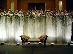 a couch sitting in front of a white curtain with flowers on it's side