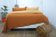 a bed with orange sheets and pillows in a white room next to a potted plant