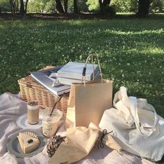 a picnic table with books and drinks on it in the park, next to a wicker basket