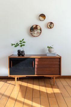 three plates mounted on the wall above a wooden cabinet with two planters and one potted plant