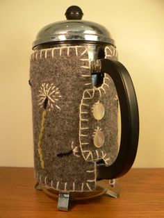 a close up of a coffee pot on a wooden table with a metal lid and handle