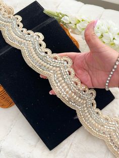 a hand is holding a gold and silver bracelet on a black velvet box with flowers in the background