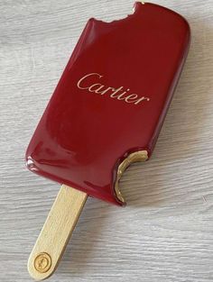 a red and gold colored ice cream on a wooden stick with the name cartier written on it