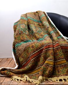 a blanket sitting on top of a wooden floor next to a black chair and white wall