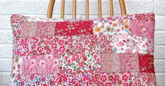 a pink and red patchwork pillow sitting on top of a wooden chair next to a white brick wall