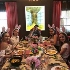 a group of people sitting at a table with bunny ears on their head and plates of food in front of them