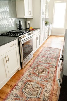 a kitchen with white cabinets and an area rug on the floor in front of the stove